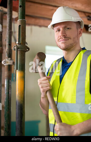 Portrait Of Construction Worker With Sledgehammer Demolishing Wall In Renovated House Stock Photo