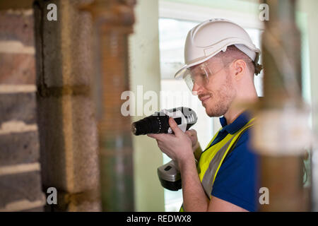 Construction Worker With Cordless Drill Drilling Wall In Renovated House Stock Photo