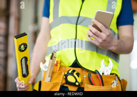 Detail Of Construction Worker On Building Site Wearing Tool Belt Using Mobile Phone Stock Photo