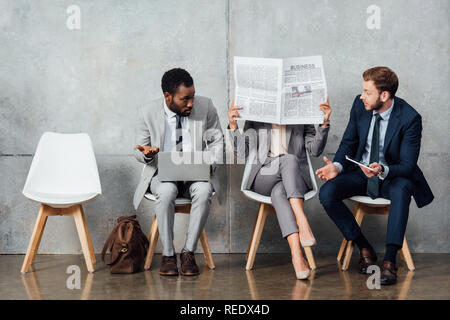 multiethnic businesspeople reading newspaper and using digital devices in waiting hall Stock Photo