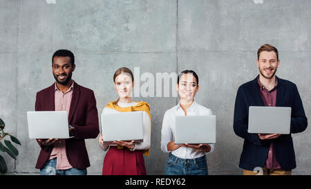 multiethnic casual businesspeople using laptops in waiting hall and looking at camera Stock Photo
