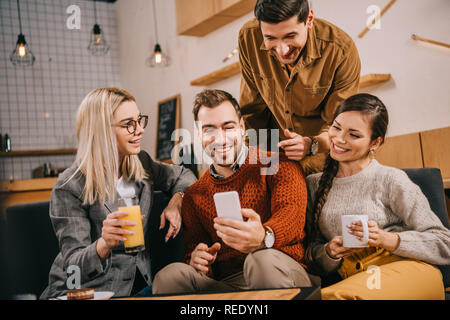 handsome man pointing with finger at smartphone near friends Stock Photo