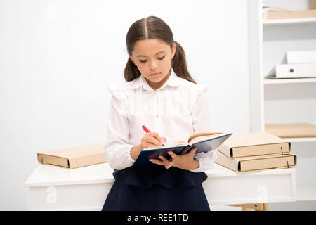 Boring task to write. How make education more interesting for first formers. Girl child hold book make note. Kid school uniform calm sad indifferent face write textbook. Indifferent about knowledge. Stock Photo