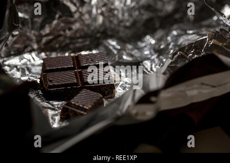 Macro photo of dark chocolate pieces in foil wrapper. Stock Photo