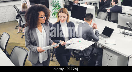 high angle view of young multiethnic businesswomen holding documents and discussing project while walking in office Stock Photo