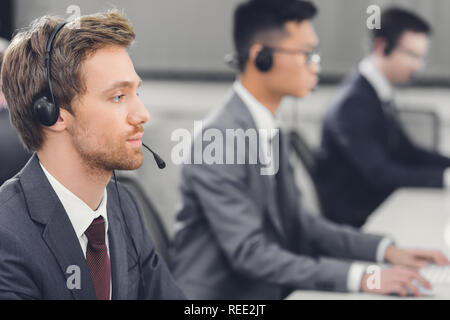 side view of focused young businessman in headset working with colleagues in call center Stock Photo
