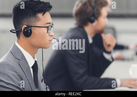 side view of focused young asian businessman in headset working with colleagues in office Stock Photo