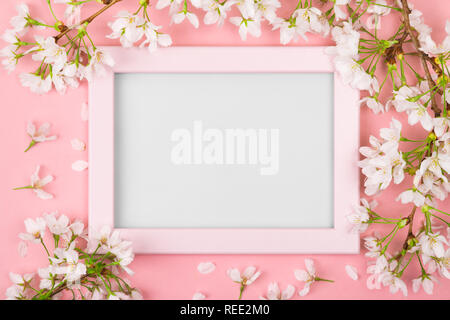 Spring background with an empty pink picture frame surrounded by white cherry blossom flowers and branches on a pink surface. Flat lay Stock Photo