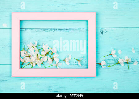 Cherry blossom flowers inside an empty pink picture frame on turquoise wooden planks. Flat lay Stock Photo