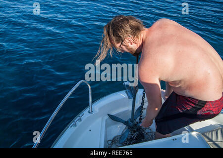 A young man on a boat pulling the rope of an anchor Stock Photo