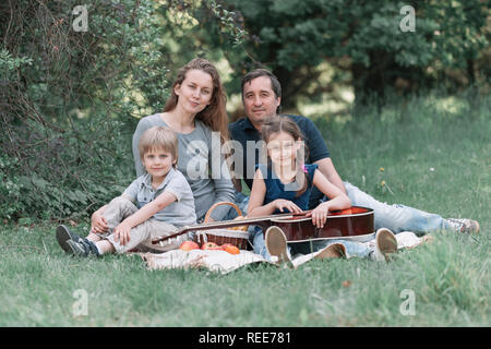 family with two children resting on the Sunny lawn in the summer Park Stock Photo