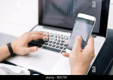 close up. the businessman uses a smartphone and a laptop in the workplace. Stock Photo