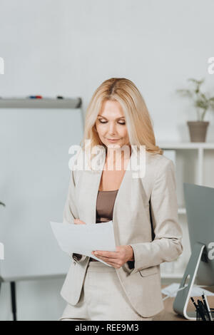 focused mature businesswoman holding paper and taking notes in office Stock Photo