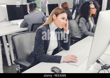 young businesswoman suffering from headache and looking at desktop computer in office Stock Photo