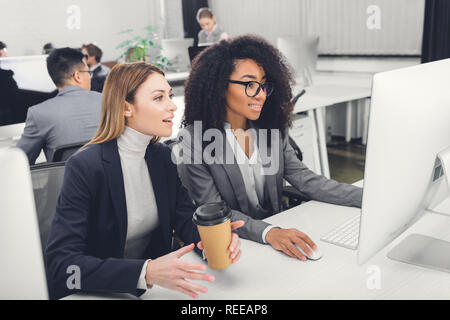 smiling young multiethnic businesswomen using desktop computer together in office Stock Photo