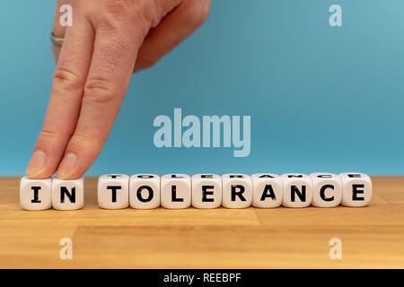 Tolerance instead of intolerance. Dice form the word intolerance, while the letters 'IN' where pushed away by a finger Stock Photo