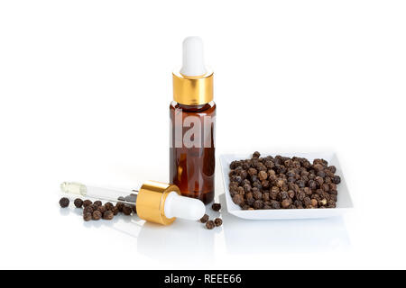 Black pepper essential oil isolated on white background. Black pepper oil bottle with dropper for beauty, skin care, wellness and medicinal purposes. Stock Photo