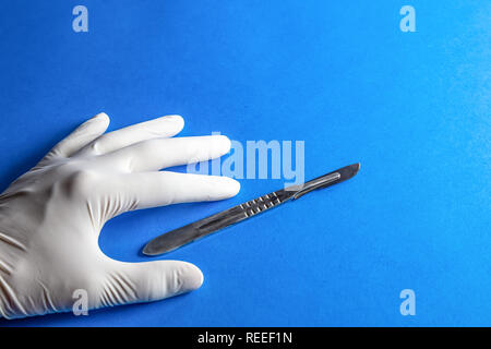 Scalpel in surgeon's hand over blue background.  Hand holding a scalpel on blue background with place for copy-space. Stock Photo