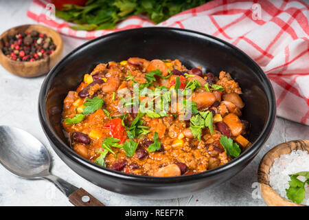 Chili con carne from meat, beans and vegetables in black plate on stone table. Traditional mexican food. Stock Photo