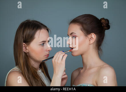 Woman makeup artist holding makeup brushes and applying lipstick on perfect fashion model lip Stock Photo