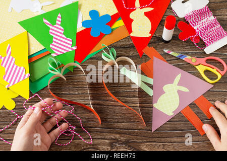 The child folds details festive Easter garland on a wooden background. Project of children's creativity, handicrafts, crafts for kids. Stock Photo
