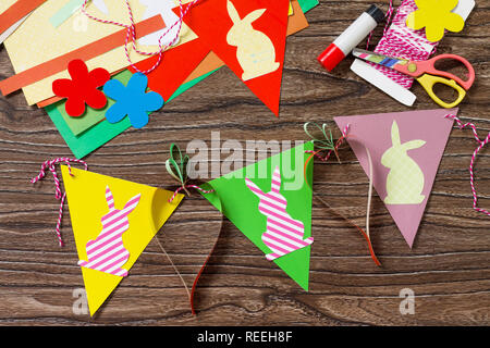 Festive Easter garland handmade with decoration of colorful rabbits and carrot on a wooden background. Handicrafts for kids. Top view flat lay backgro Stock Photo