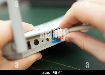 Man plugging internet cable into wifi router. Stock Photo
