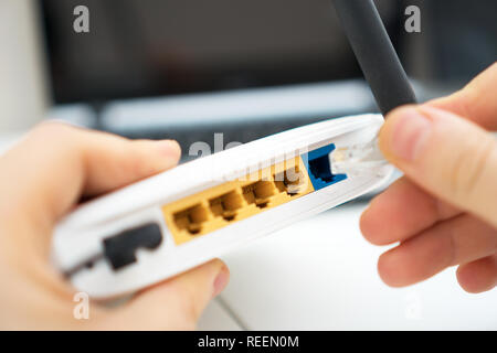 Man plugging internet cable into wifi router. Stock Photo