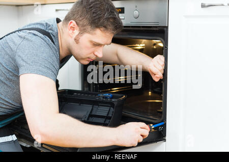 Professional handyman in overalls repairing domestic oven in the kitchen. Stock Photo