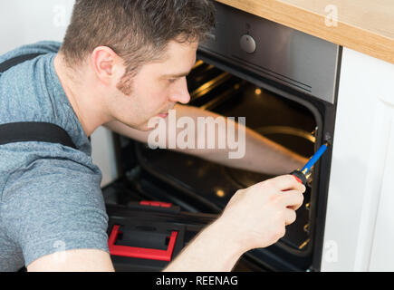 Professional handyman in overalls repairing domestic oven in the kitchen. Stock Photo