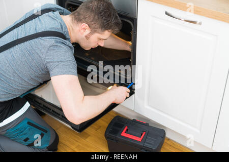 Professional handyman in overalls repairing domestic oven in the kitchen. Stock Photo