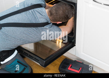 Professional handyman in overalls repairing domestic oven in the kitchen. Stock Photo