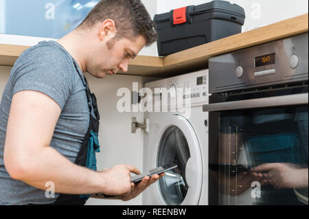 Handyman doing inspection of washing machine in the kitchen. Stock Photo