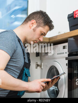 Handyman doing inspection of washing machine in the kitchen. Stock Photo