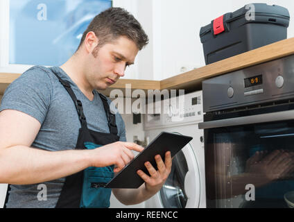 Handyman doing inspection of washing machine in the kitchen. Stock Photo