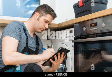Handyman doing inspection of washing machine in the kitchen. Stock Photo