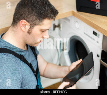 Handyman doing inspection of washing machine in the kitchen. Stock Photo