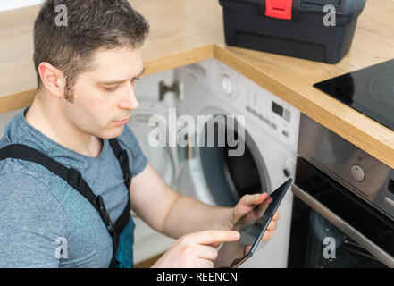 Handyman doing inspection of washing machine in the kitchen. Stock Photo