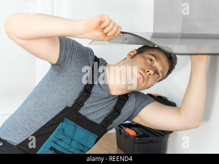 Handsome foreman fixing exhaust hood in the kitchen. Stock Photo