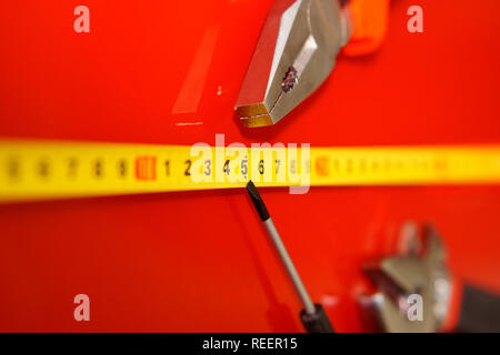 Pliers, tape measure and screwdriver-tap lie on the red polished surface in the auto repair shop. Tools mechanics. Performance of work. Stock Photo