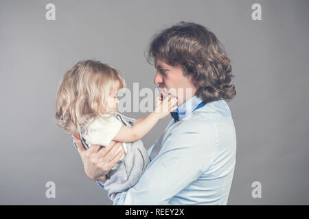 Happy smiling father holding on hands preschool daughter, looking at each other, father standing on grey studio background together with little girl.  Stock Photo