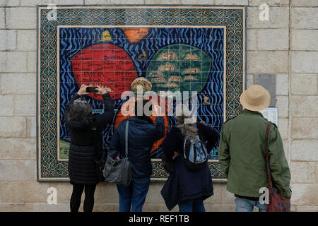 Tourist looking at a mosaic model by Armenian ceramicist Arman Darian depicting the Bunting Clover Leaf Map, also known as The World in a Cloverleaf, an historic mappa mundi drawn by the German Protestant pastor, Heinrich Bünting. in which Jerusalem is in the centre of the map surrounded by the three continents, comprising three leaves of a clover shape installed on the fence of Safra Square at the site of Jerusalem's city hall. Israel Stock Photo