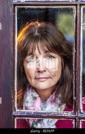 Model released attractive, single woman, looking out of a window Stock Photo