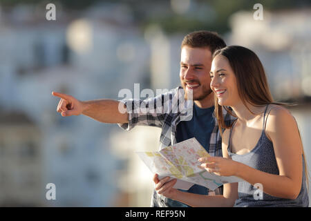 Happy couple of tourists holding paper map pointing away in a town on vacation Stock Photo