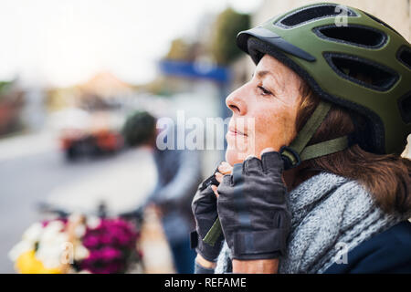 Active senior woman standing outdoors in town, putting on a bike helmet. Copy space. Stock Photo