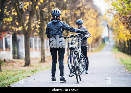 Active senior couple with electrobikes standing outdoors on a road in park. Stock Photo