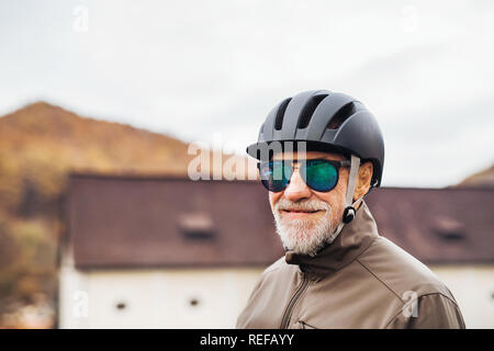 Active senior man with bike helmet and sunglasses standing outdoors in town. Stock Photo
