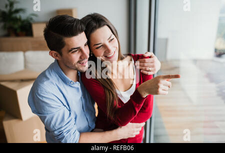 Young couple with cardboard boxes moving in a new home, looking out of window. Stock Photo