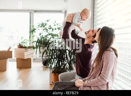 A portrait of young couple with a baby and cardboard boxes moving in a new home. Stock Photo