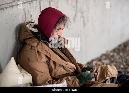 Homeless beggar man sitting outdoors in city asking for money donation. Stock Photo
